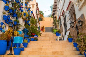 Narrow,Street,With,Steps,,White,Houses,And,Blue,Potted,Plants